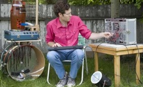 Chad Vangaalen playing a bunch of instruments in a yard
